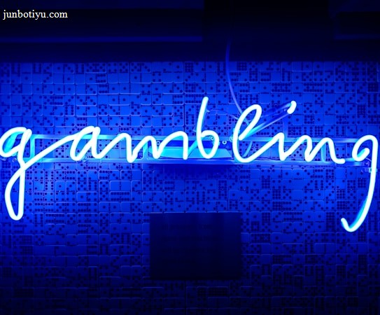 A bright blue neon sign spells out the word 'gambling' in cursive script. The background features a textured wall covered in domino tiles, also illuminated by the blue light, creating a vivid and visually striking scene.